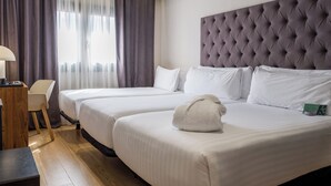 Une chambre d’hôtel avec deux lits, une tête de lit capitonnée, un bureau avec une lampe et une chaise.