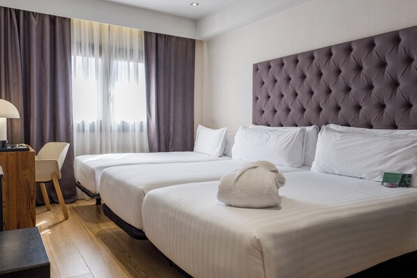Una camera d'albergo con due letti, una testiera trapuntata, una scrivania con una lampada e una sedia.