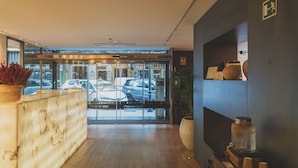 Un espace d’accueil d’hôtel avec un comptoir en marbre, une porte d’entrée en verre et une plante placée sur le côté gauche.