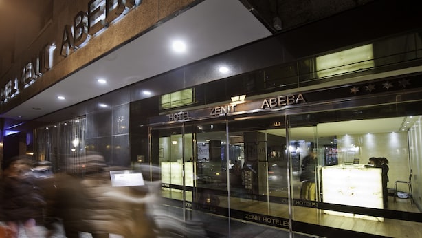 La façade extérieure de l’hôtel Zenit, avec sa devanture en verre et ses enseignes lumineuses.