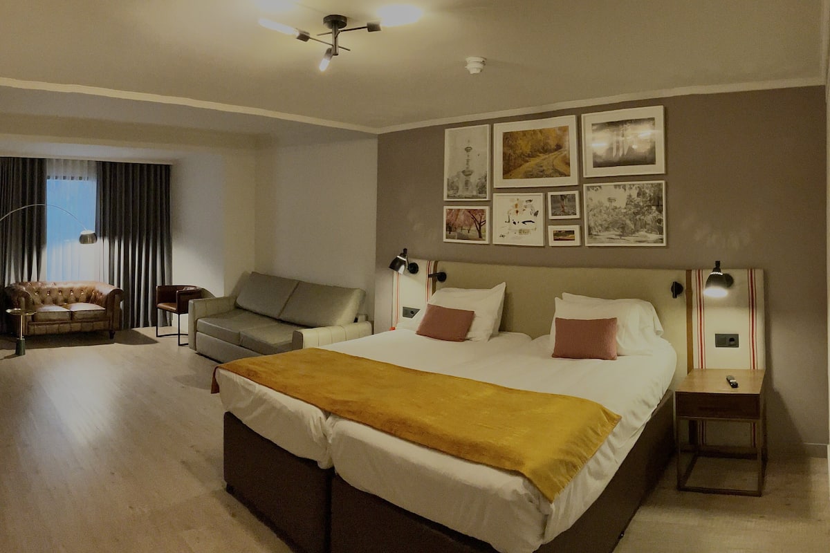 A hotel room with a large bed, a sofa, a desk, and a ceiling fan.
