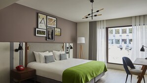 Una habitación de hotel con una cama grande, un escritorio con una silla, un teléfono rojo y una ventana con cortinas.