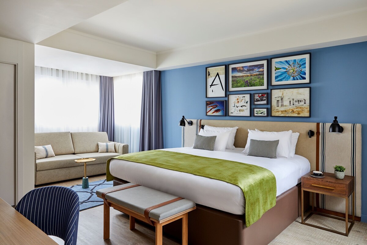 A hotel room with a bed, bedside table, lamp, and a sofa.