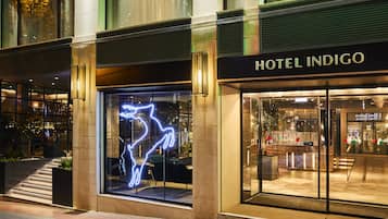 Hotel Indigo features a striking glass facade and a contemporary entrance marked by a neon sign.