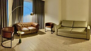 Una sala de estar con un sofá de cuero marrón, un sillón beige y una lámpara de pie.