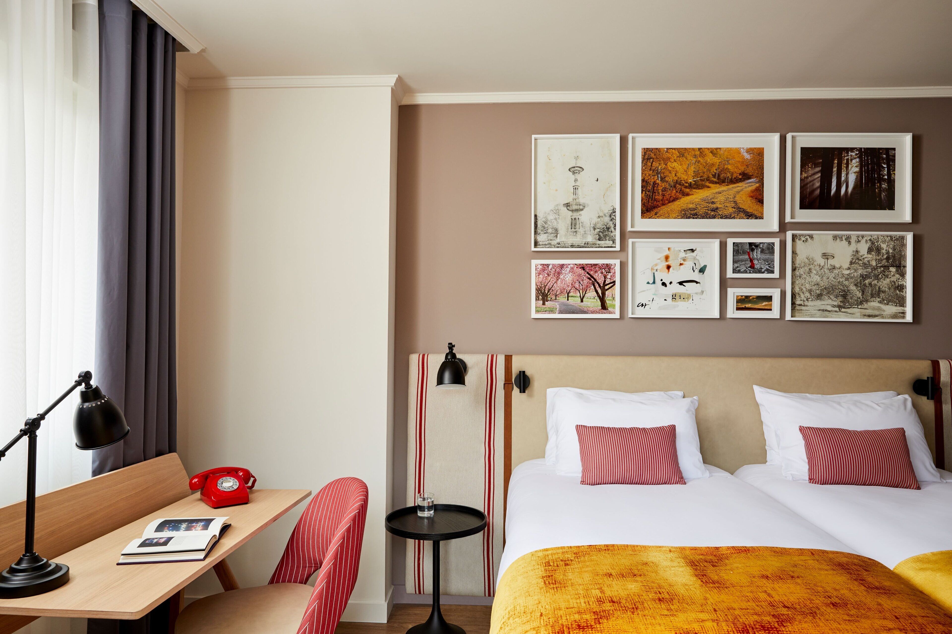 Habitación de hotel con cama, mesitas de noche, escritorio, silla y un muro con cuadros.