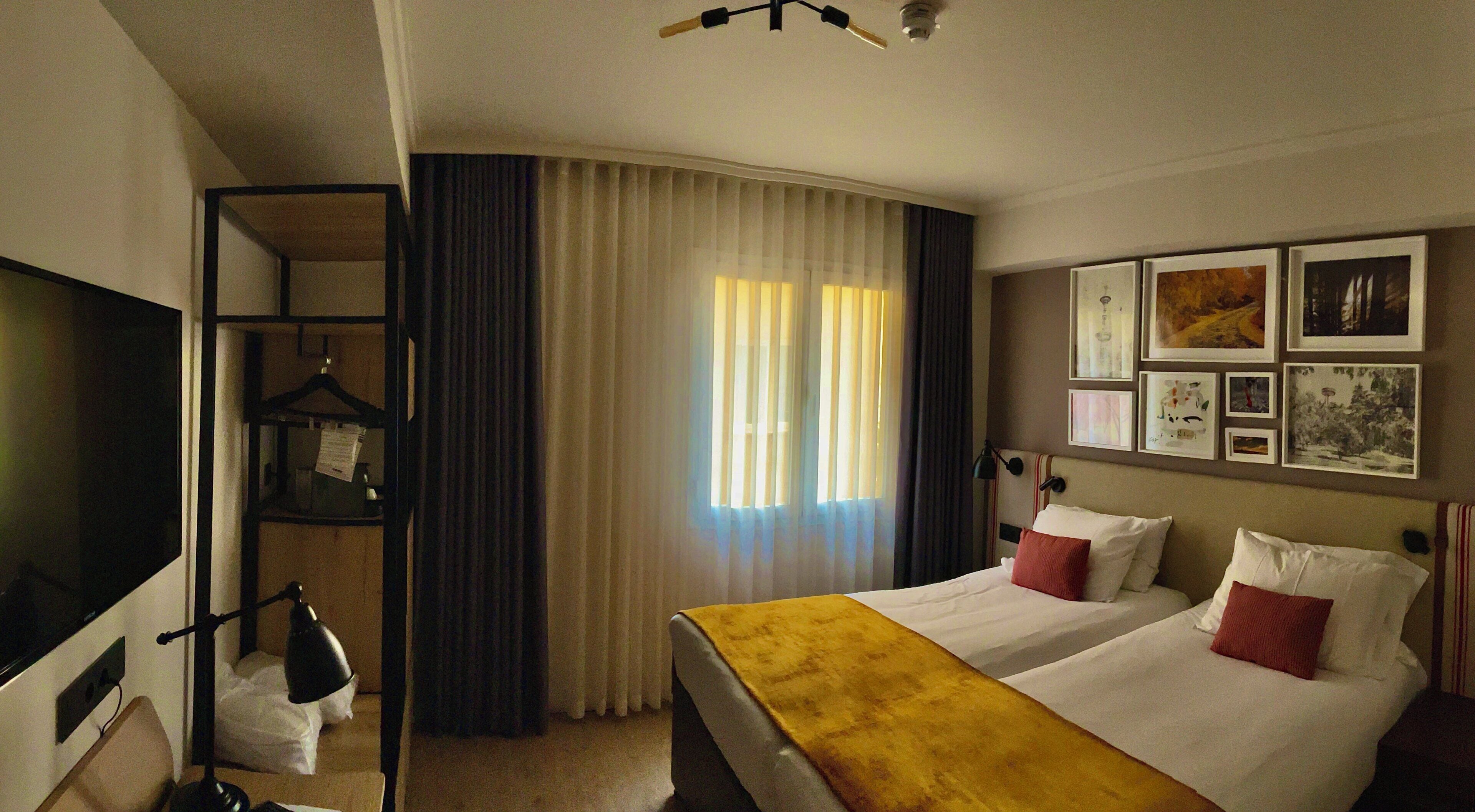 Habitació d'hotel amb un llit, una televisió, escriptori, cadira, armari i finestra amb cortines.