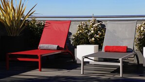 Un área de lounge en la azotea con dos tumbonas, una con cojín rojo y la otra con cojín blanco.