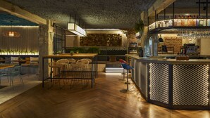 Zona de bar con suelo de madera, una barra con diseño iluminado y un patrón, y un área de estar con sillas de mimbre y una mesa.
