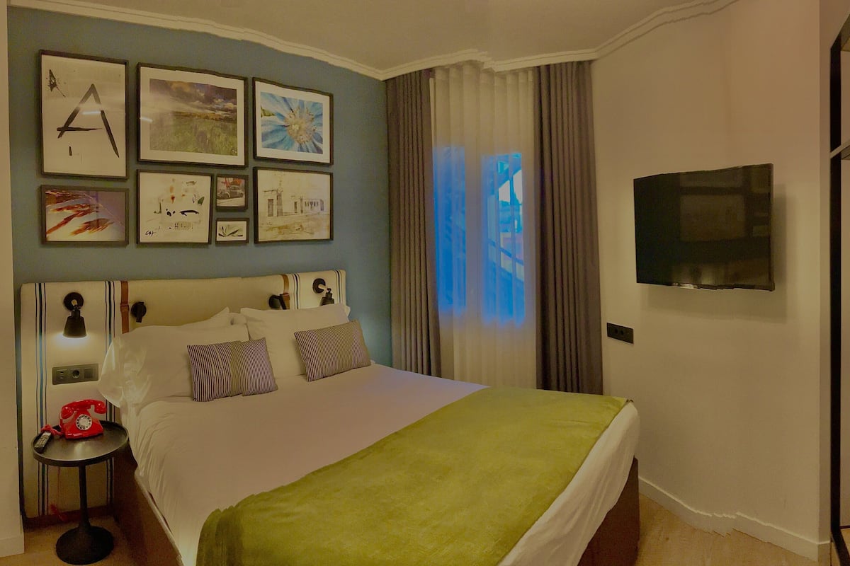 A hotel room with a bed, a TV, a desk with a telephone, and a bunk bed.