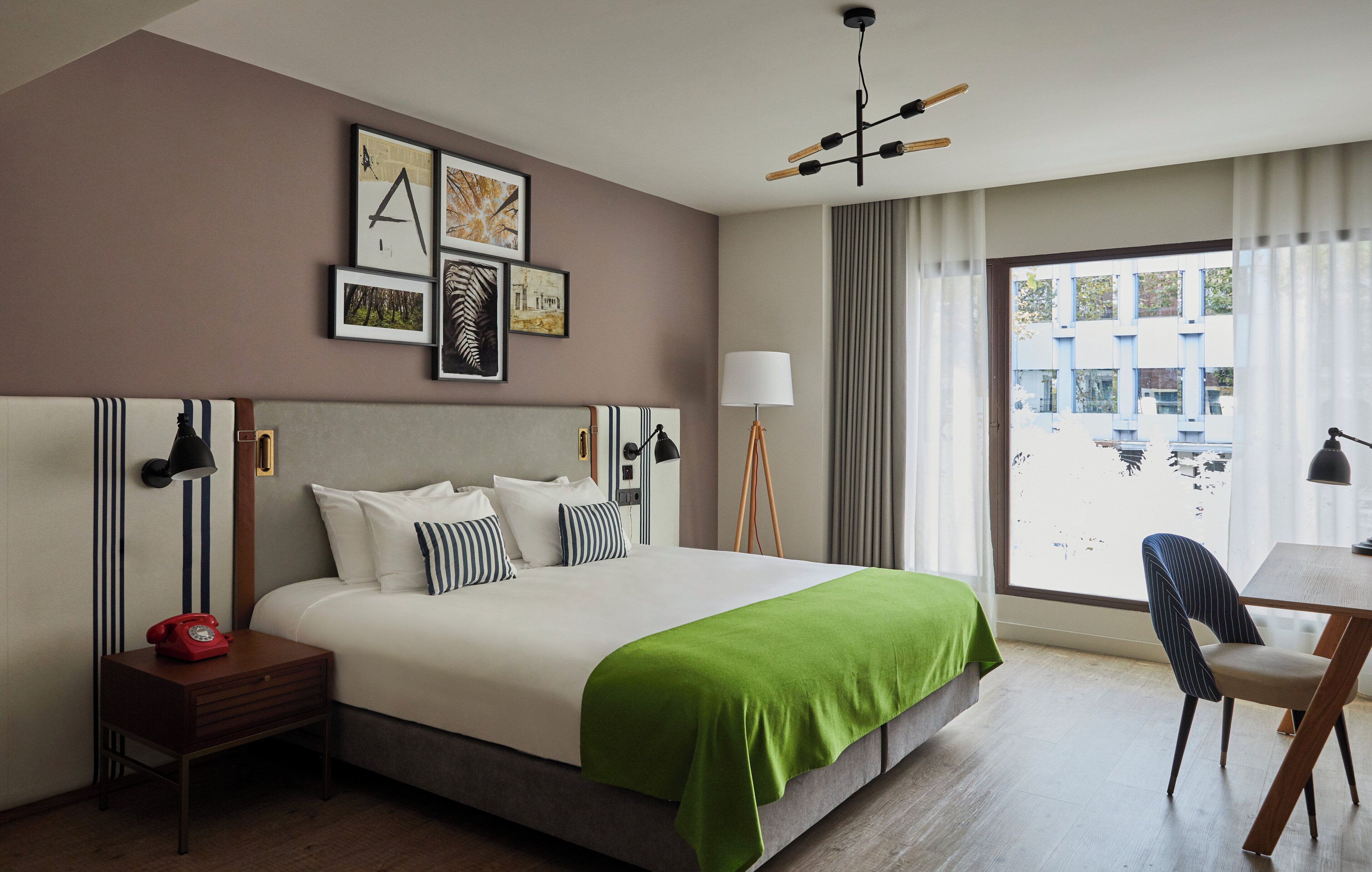 Una habitació d'hotel amb un llit gran, un escriptori, una cadira, una taula de nit amb una làmpada, un telèfon i obres d'art a la paret.