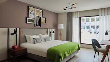 Una habitació d'hotel amb un llit gran, un escriptori, una cadira, una taula de nit amb una làmpada, un telèfon i obres d'art a la paret.