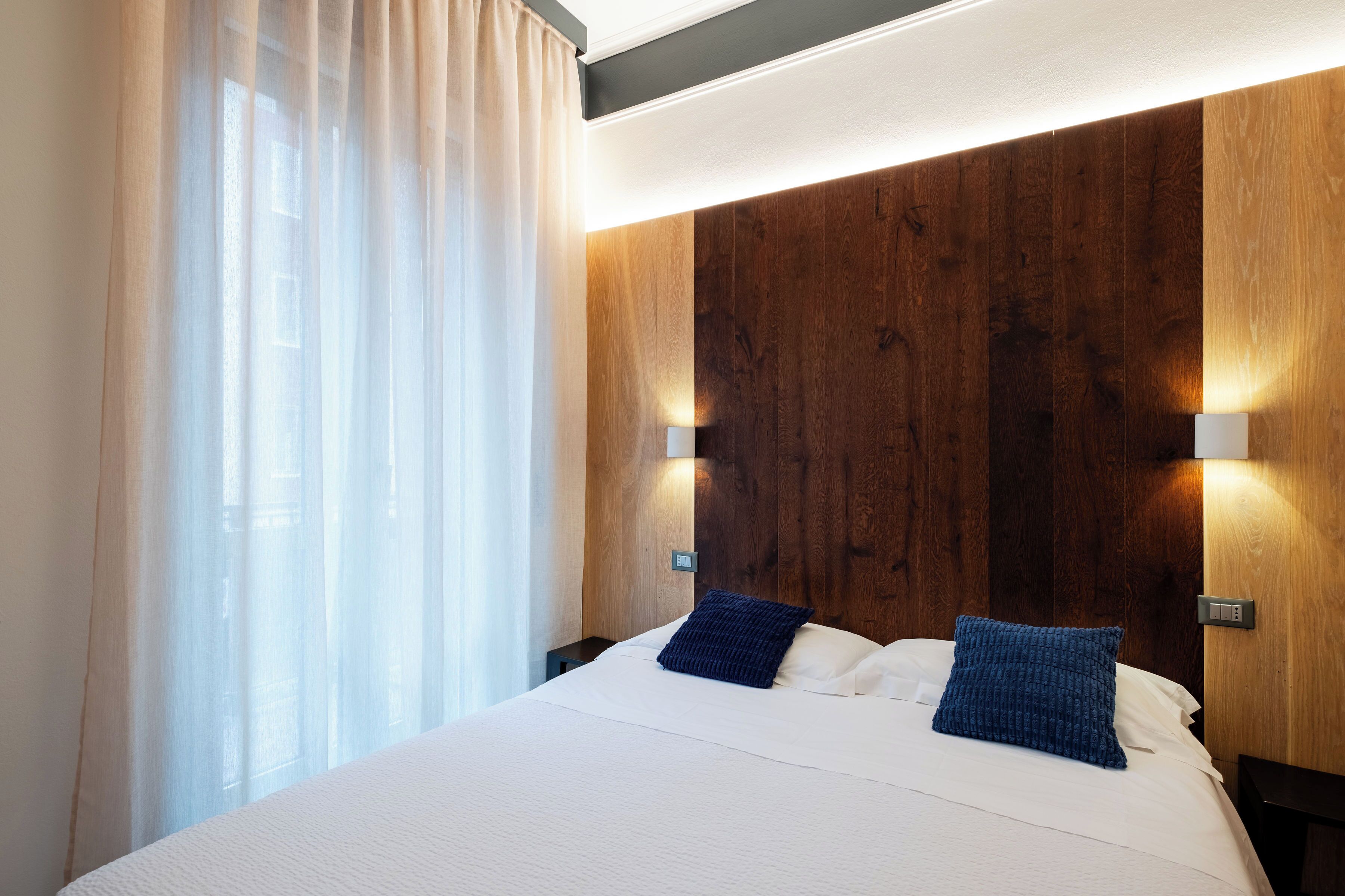 A modern hotel room with a large bed, wooden headboard, and two bedside lamps.