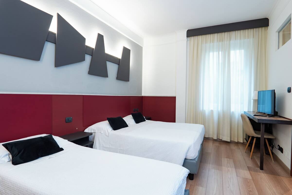 Ein Hotelzimmer mit zwei Betten, einem Schreibtisch und einem großen, abstrakten Kunstwerk an der Wand.