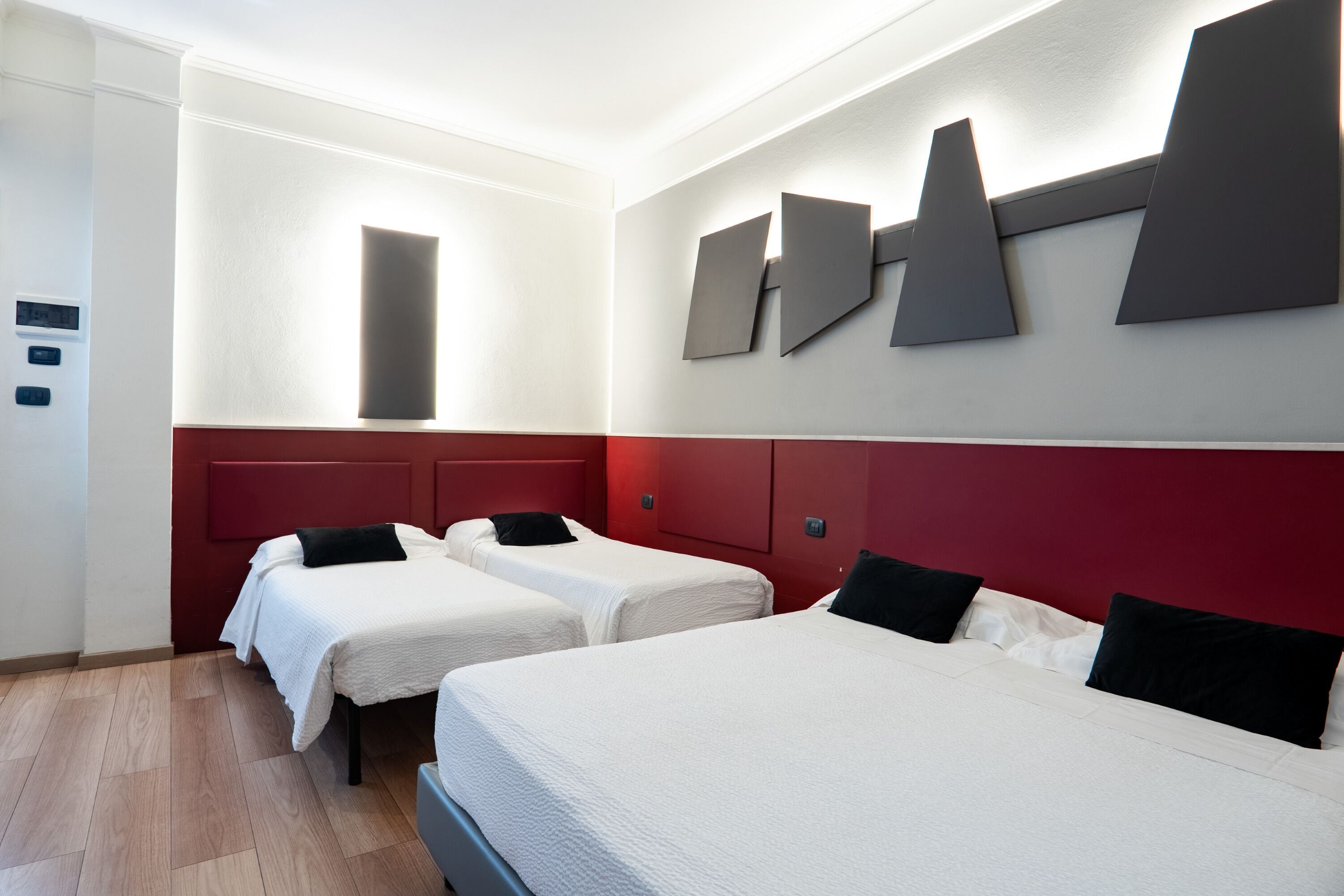 Habitación de hotel con dos camas, una pared de acento roja y un diseño moderno.
