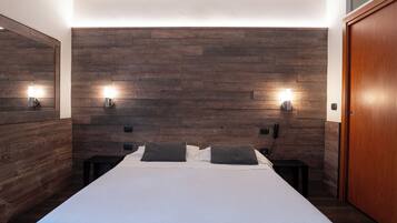 A modern bedroom with a large bed, wooden headboard, bedside lamps, and a wooden wardrobe.