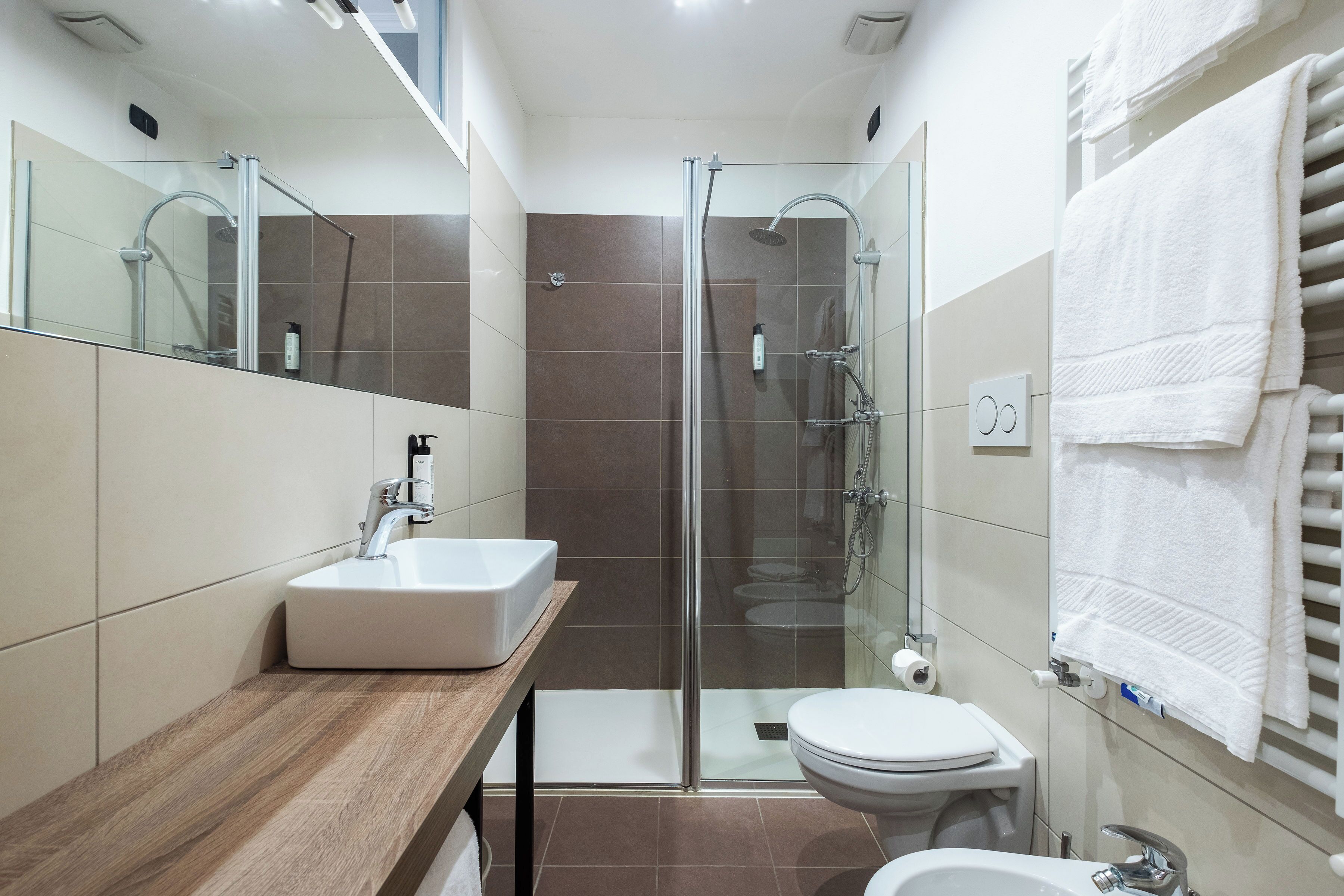 A modern bathroom with a glass-enclosed shower, a wooden vanity, a white sink, and a toilet.