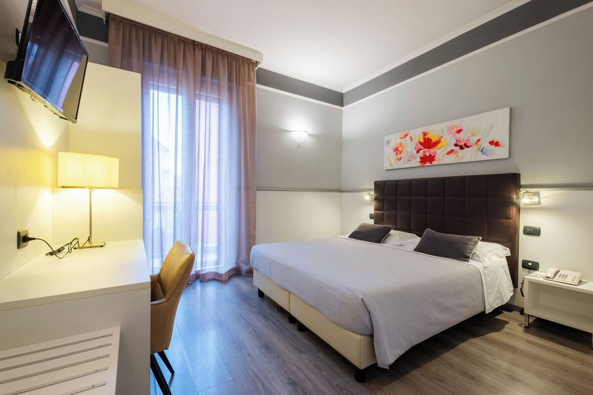 Ein Hotelzimmer mit Bett, Schreibtisch, Stuhl, Fernseher und einem Bild an der Wand.