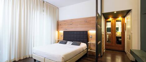 A hotel room with a large bed, wooden headboard, bedside tables, and a bench.