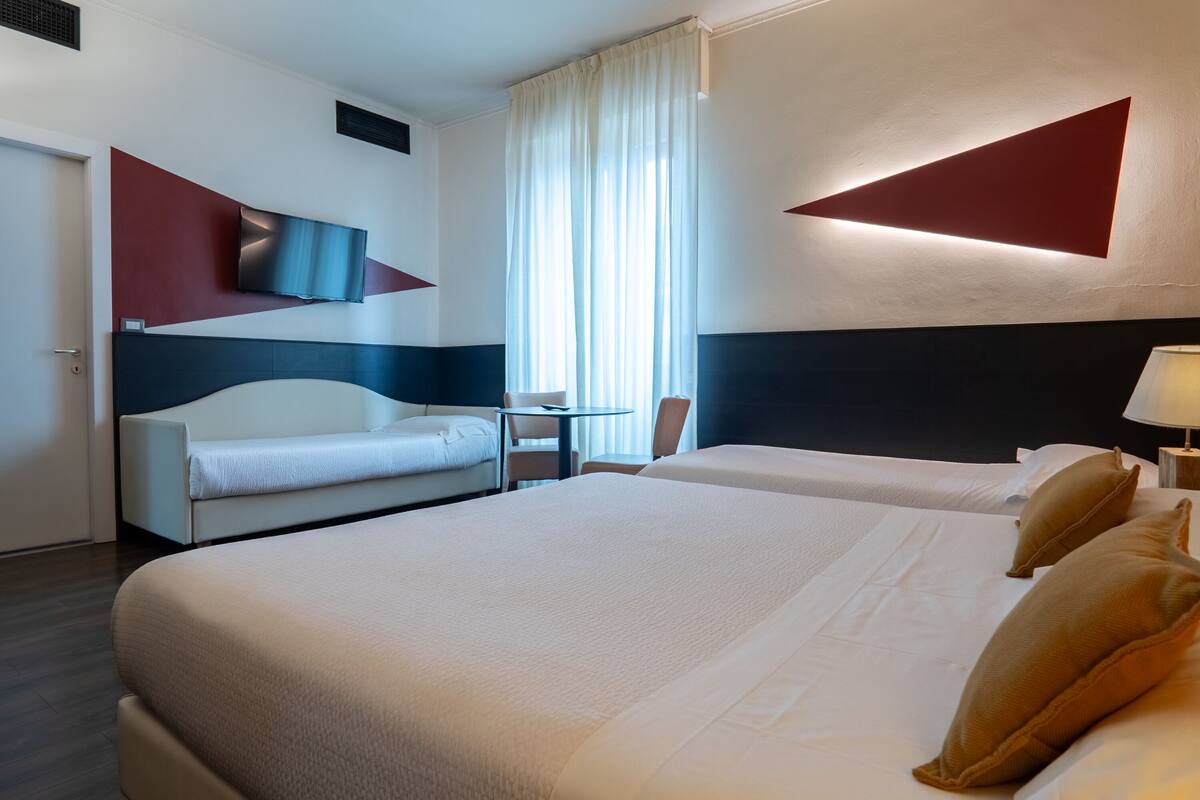 Ein Hotelzimmer mit zwei Betten, einem an der Wand befestigten Fernseher, einem kleinen Tisch und einem Stuhl.