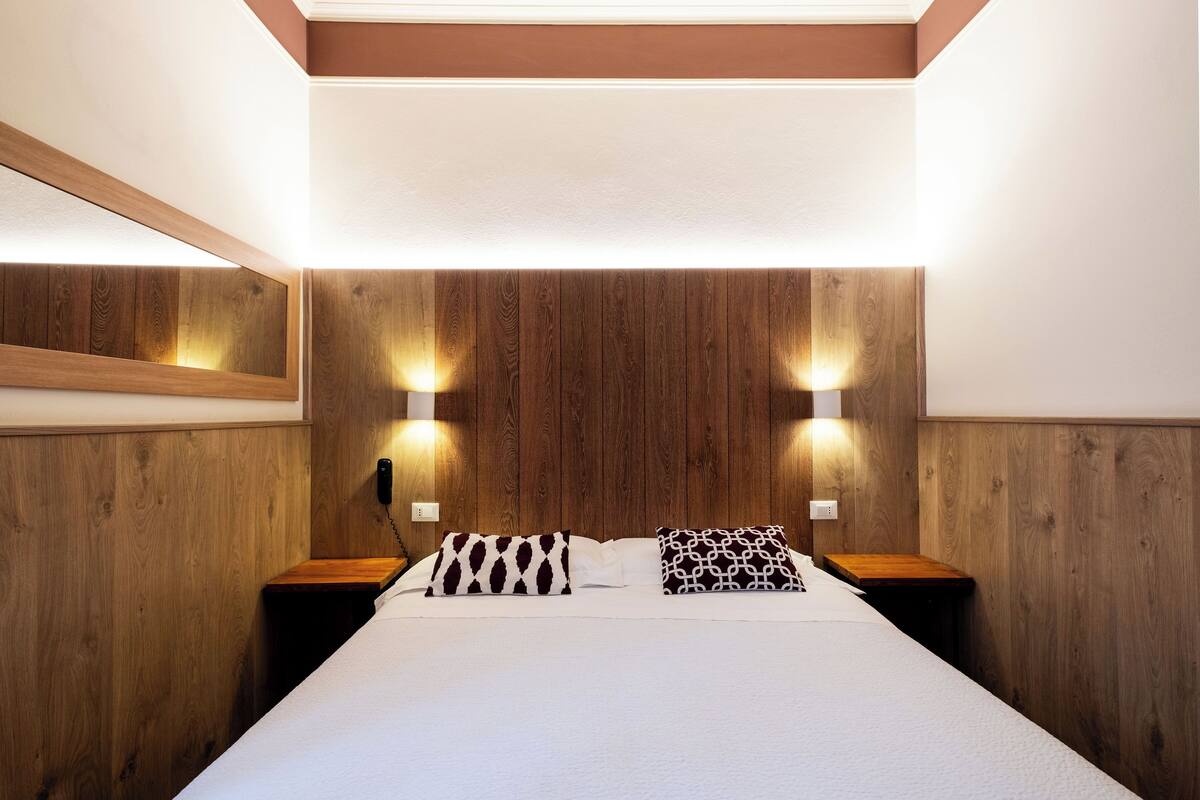 Ein ordentlich bezogenes Bett mit zwei Kissen, einem hölzernen Kopfteil und zwei Wandleuchten.
