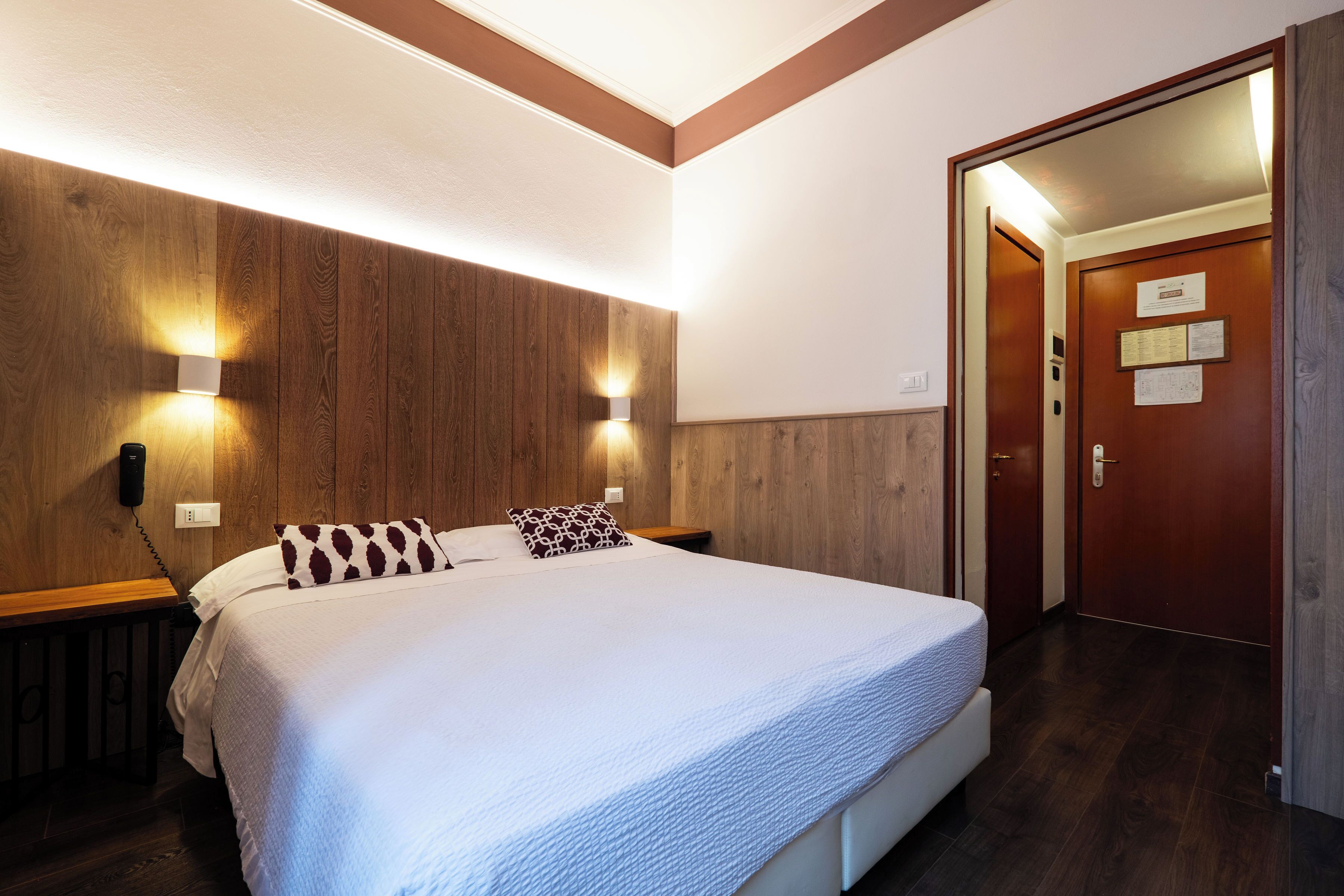 A hotel room with a large bed, wooden panel walls, two bedside lamps, and a door with a sign.