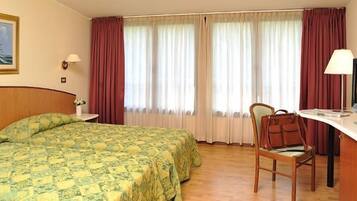 A hotel room with a bed, a desk with a TV, and a chair.