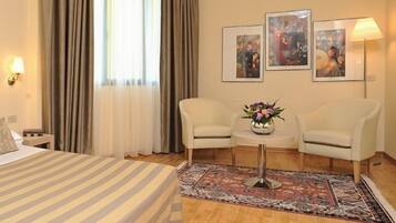 A hotel room with a large bed, two chairs, a small table with a vase, and two framed pictures on the wall.