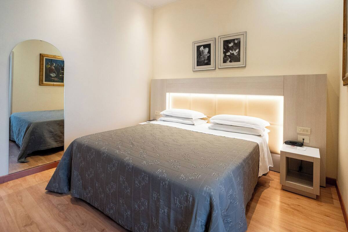 A hotel room with a large bed, a bedside table, a nightstand, and a mirror.
