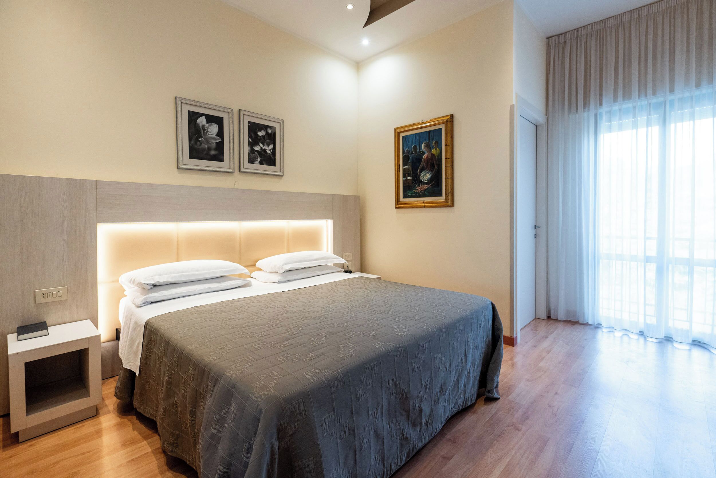 Un dormitorio ordenado con una cama grande, una mesita de noche y una mesilla auxiliar. Hay tres cuadros enmarcados en la pared.