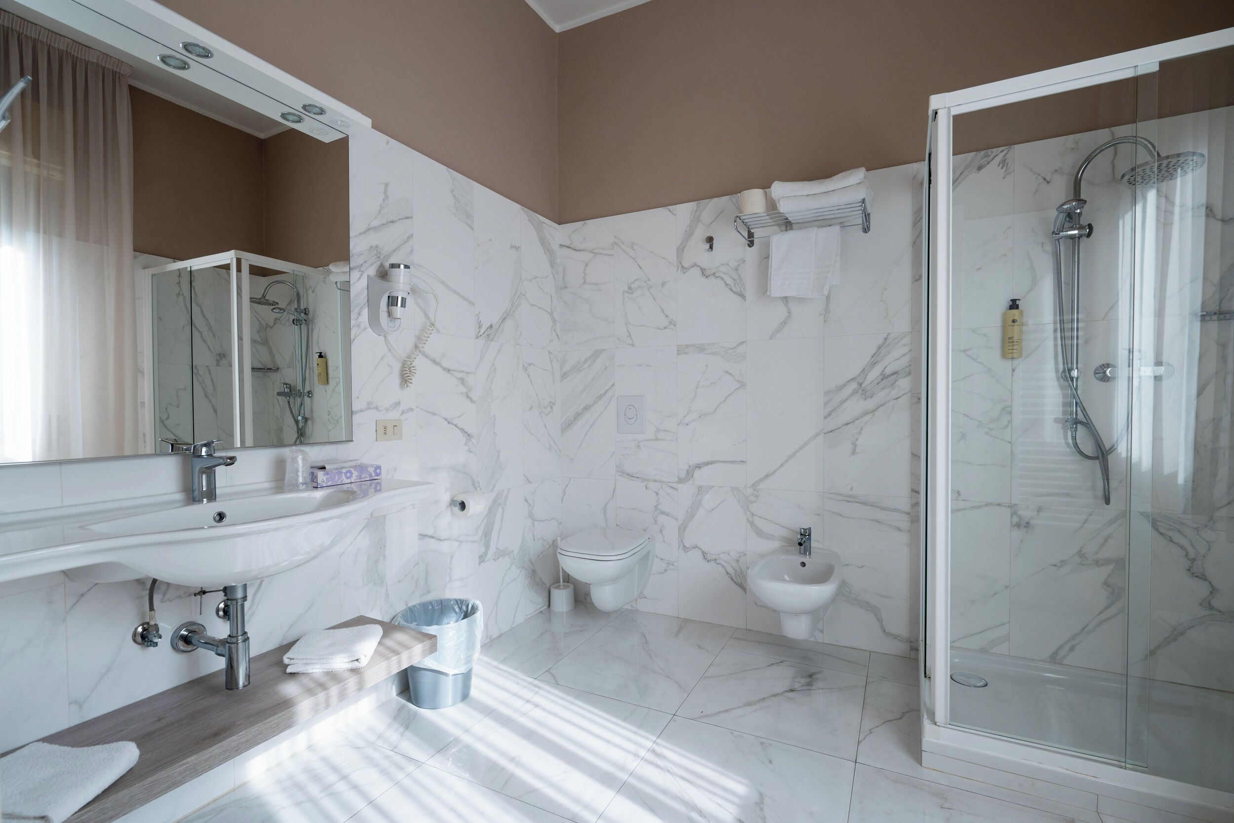 Un baño moderno con lavamanos de mármol, cabina de ducha con vidrio y un bidé.