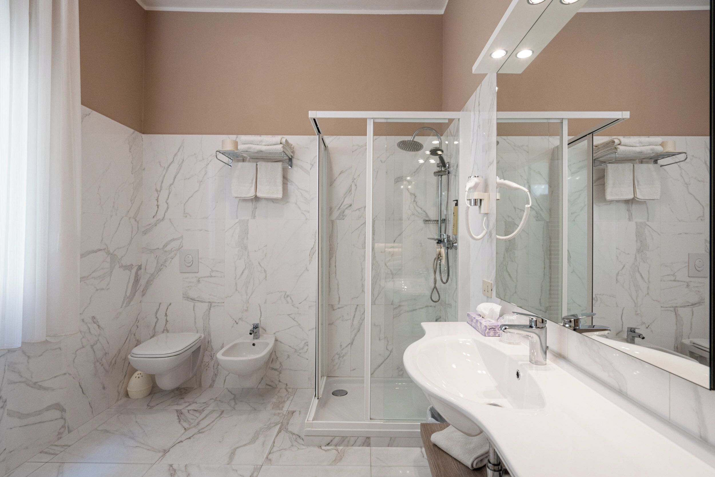 A modern bathroom with a glass-enclosed shower, a white sink, and a bidet.