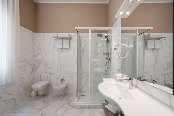 Un baño moderno con ducha de vidrio, lavamanos blanco y bidé.
