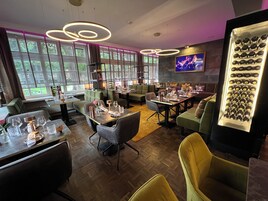 Ein modernes Restaurant mit grünen Sitzmöbeln, Holztischen und einer Weinauslage.