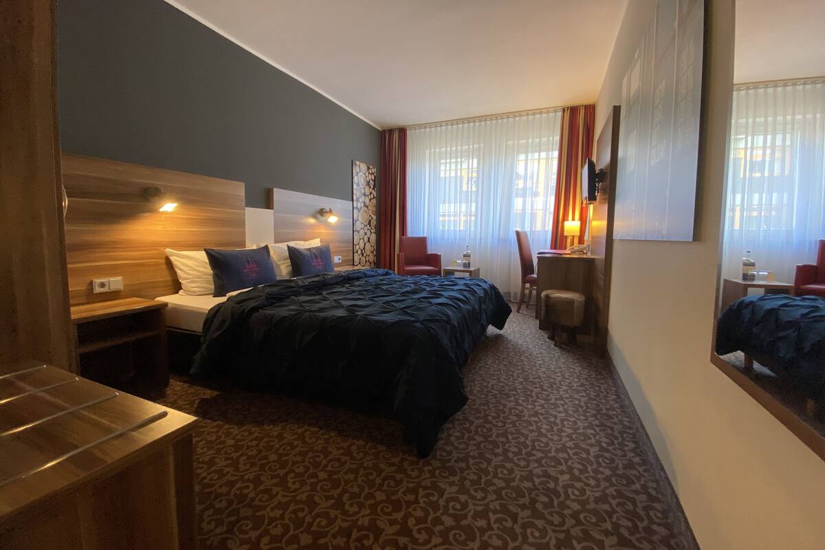 Habitación de hotel con cama, mesita de noche, silla, escritorio y un espejo grande.