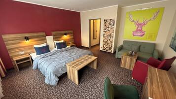 A hotel room with a bed, bedside tables, a bench, a sofa, a small table, and a wall with a deer painting.