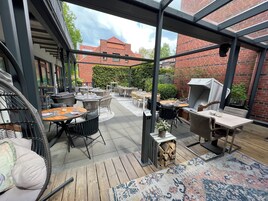 Eine Terrasse im Freien mit mehreren Tischen, Stühlen, einem Grill und einem Holzdeck.