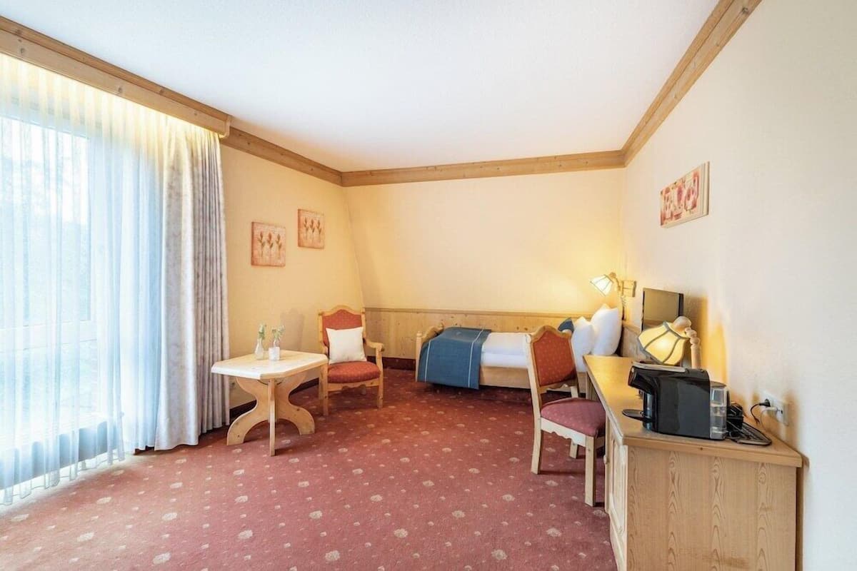Una habitación con una cama, un escritorio, una silla, una mesa y una ventana con cortinas.