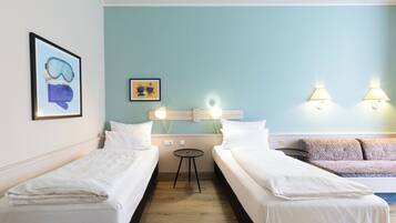 A hotel room with two single beds, a small table, a sofa, and wall-mounted lights.