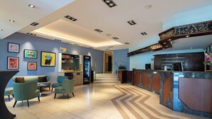 Un hall de hotel con mostrador de recepción, zona de estar y una escalera que lleva a otras plantas.
