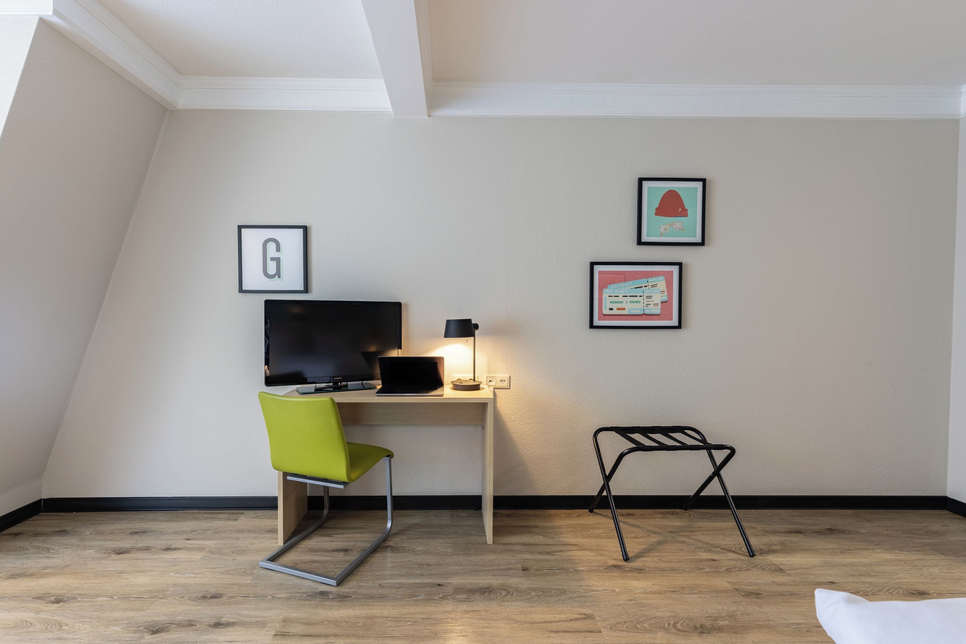 Una habitación con un escritorio, una silla, un televisor y cuadros en la pared.