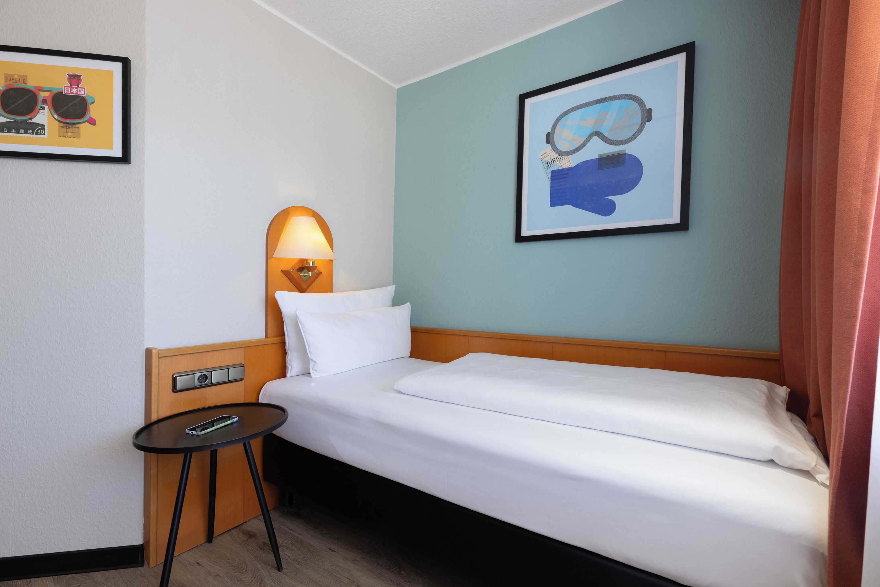 A hotel room with a bed, a bedside table with a lamp, and a framed picture on the wall.