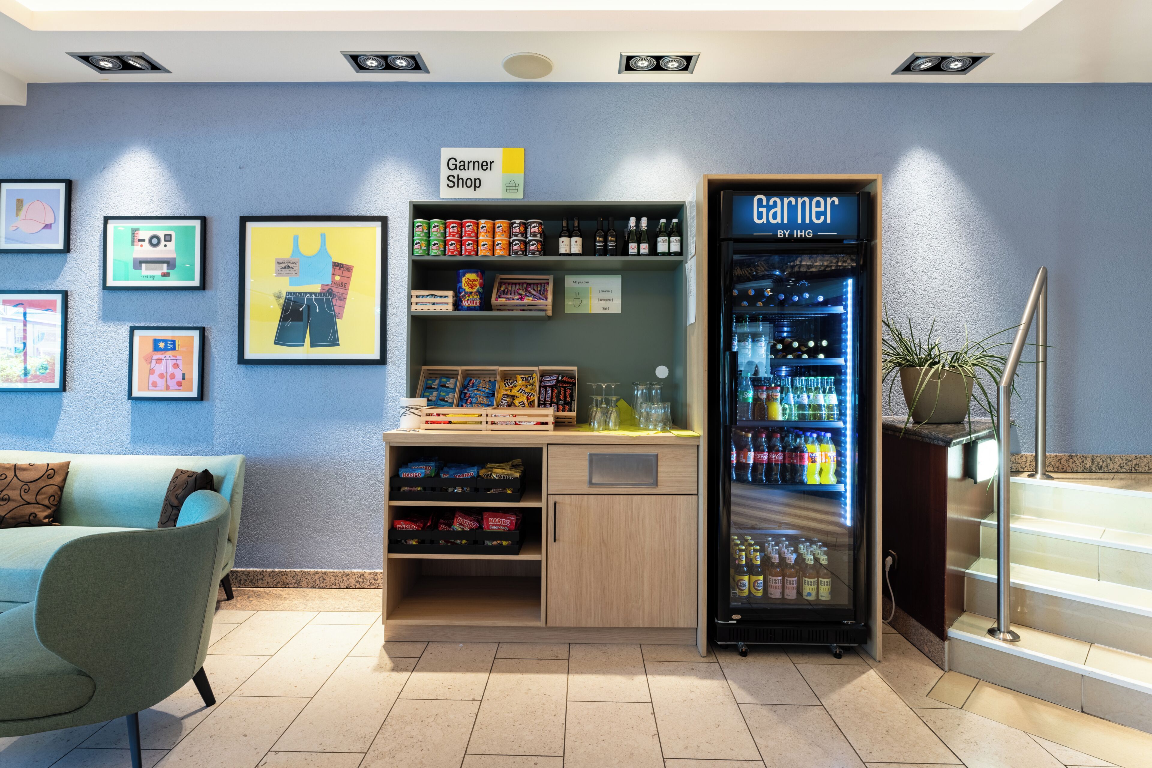 Un hall d’hôtel comprenant un magasin Garner, un réfrigérateur pour boissons, un canapé et des tableaux encadrés accrochés au mur.