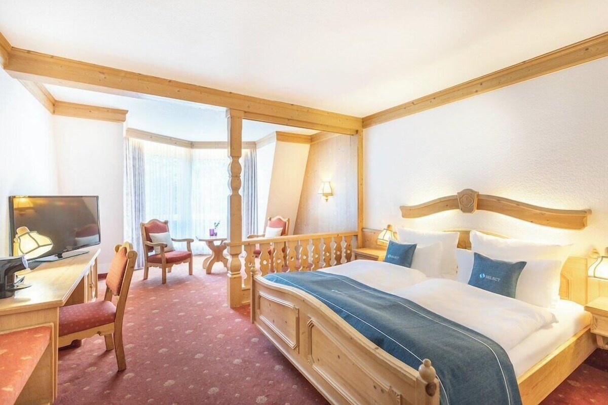 Een hotelkamer met een houten bed, een bureau met televisie, een stoel en een raam met gordijnen.