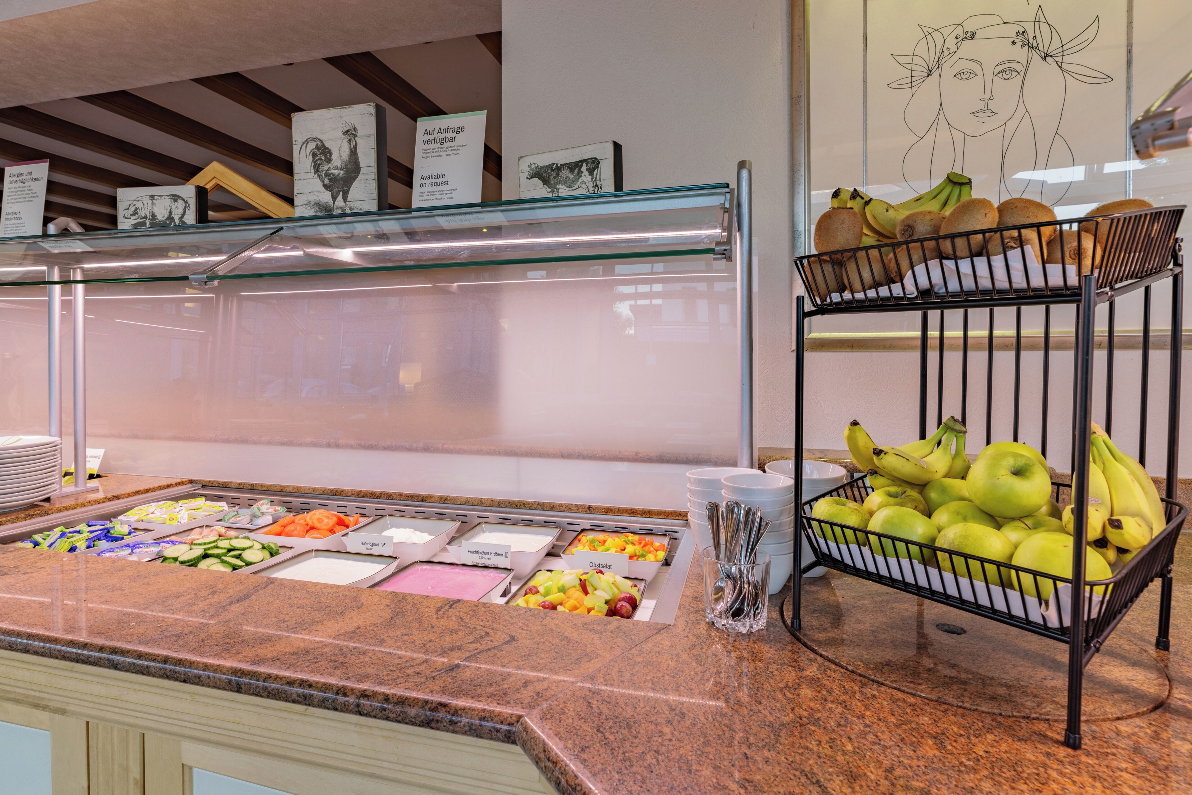 Un bufé con diversas opciones de comida, una cesta de frutas y una pared decorada con obras de arte.