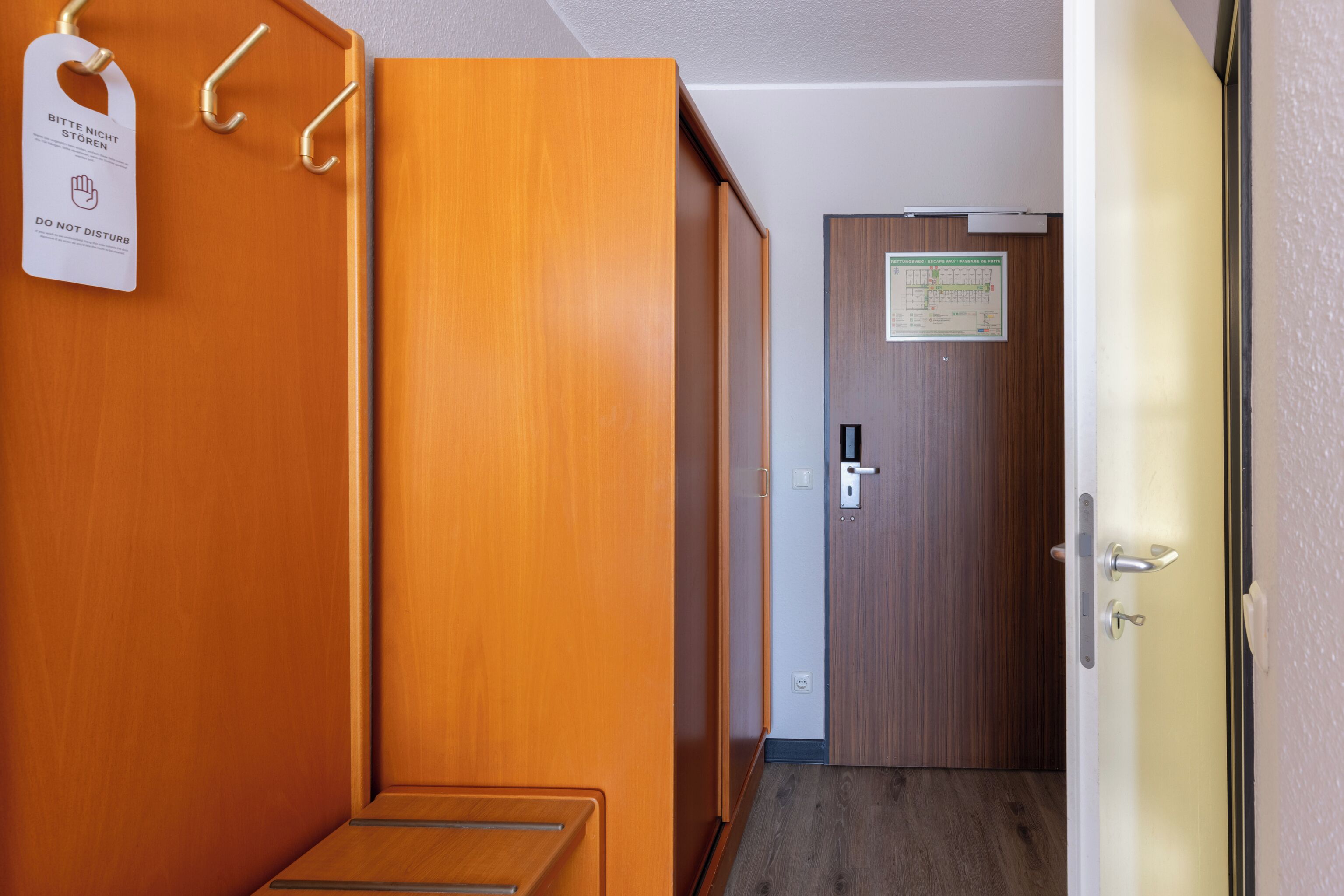 A hotel corridor with wooden walls, a coat rack, a door with a sign, and a bench.