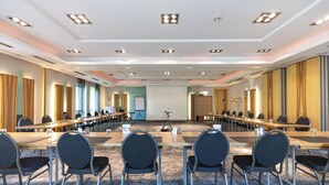 Un salón de conferencias con largas mesas, sillas y una pantalla de proyector.