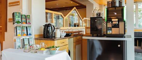 A kitchen with a coffee machine, a refrigerator, and a table with a white tablecloth.