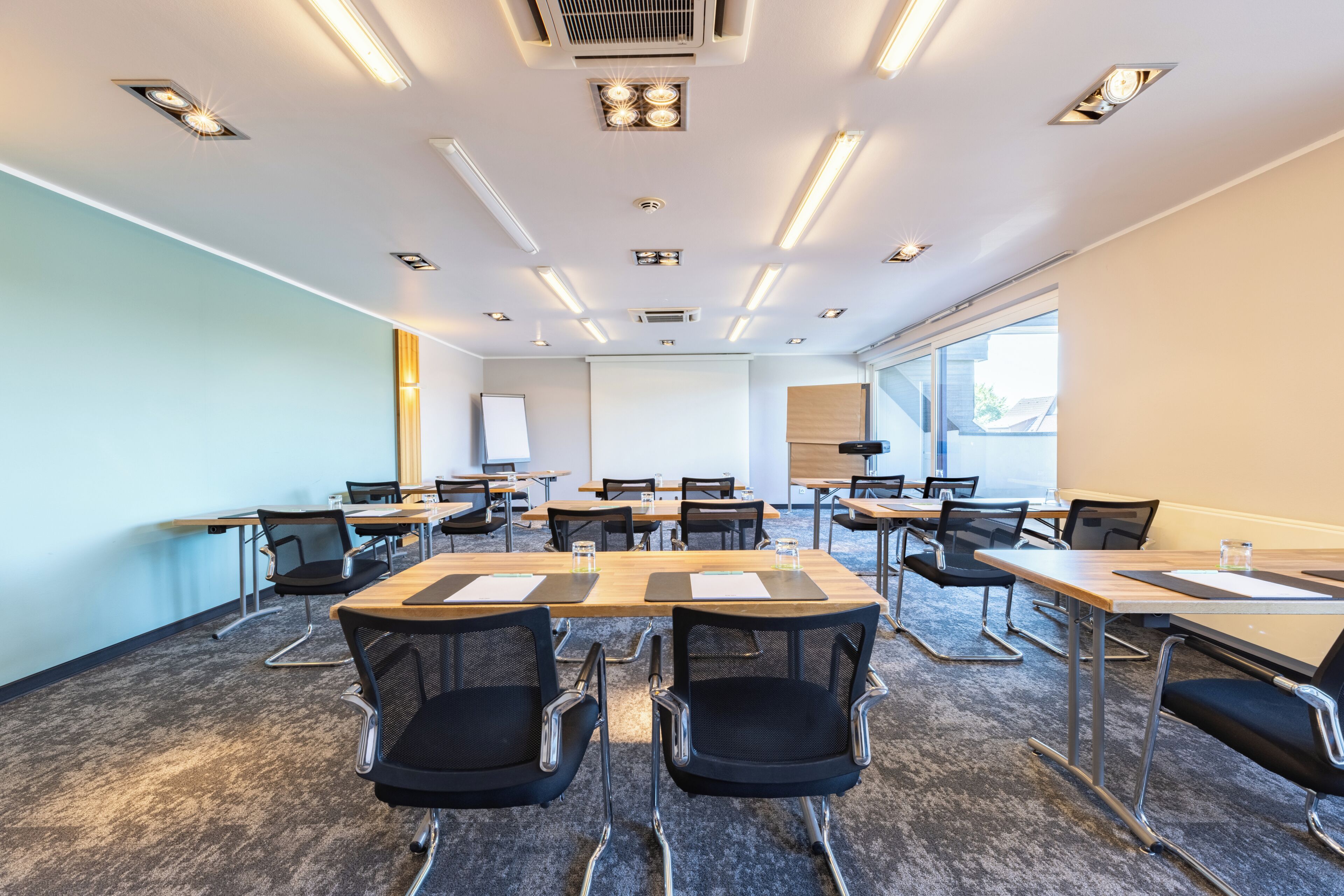 A conference room with multiple tables, chairs, and a projector screen.
