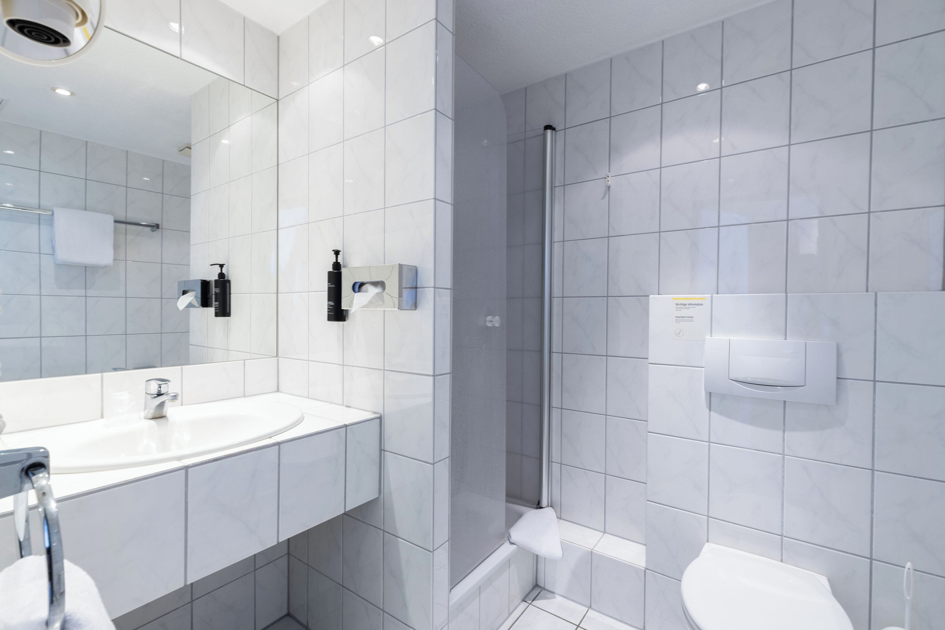Et moderne badeværelse med et stort spejl, en vask, en bruser og et toilet.